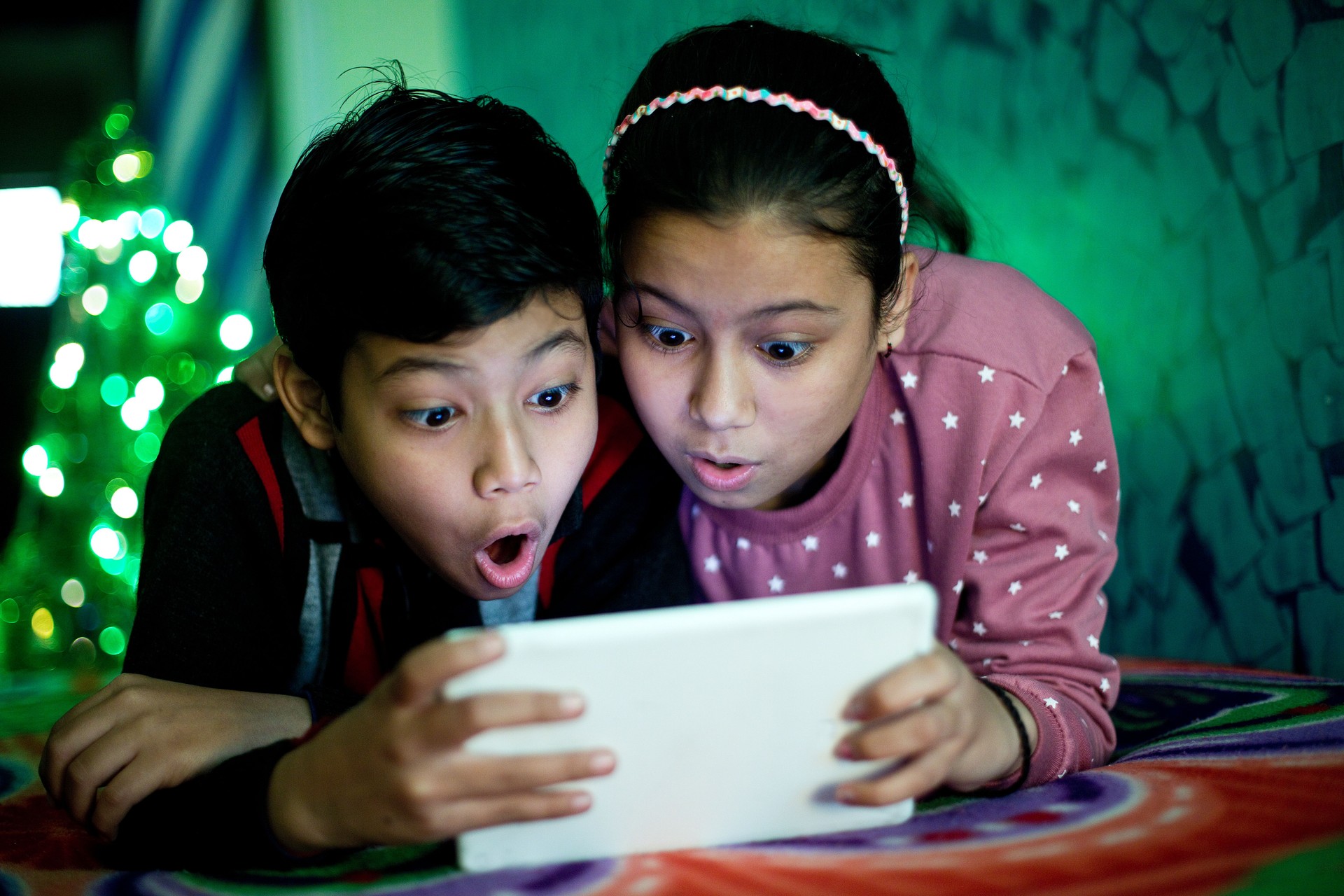 Siblings using digital tablet in bed
